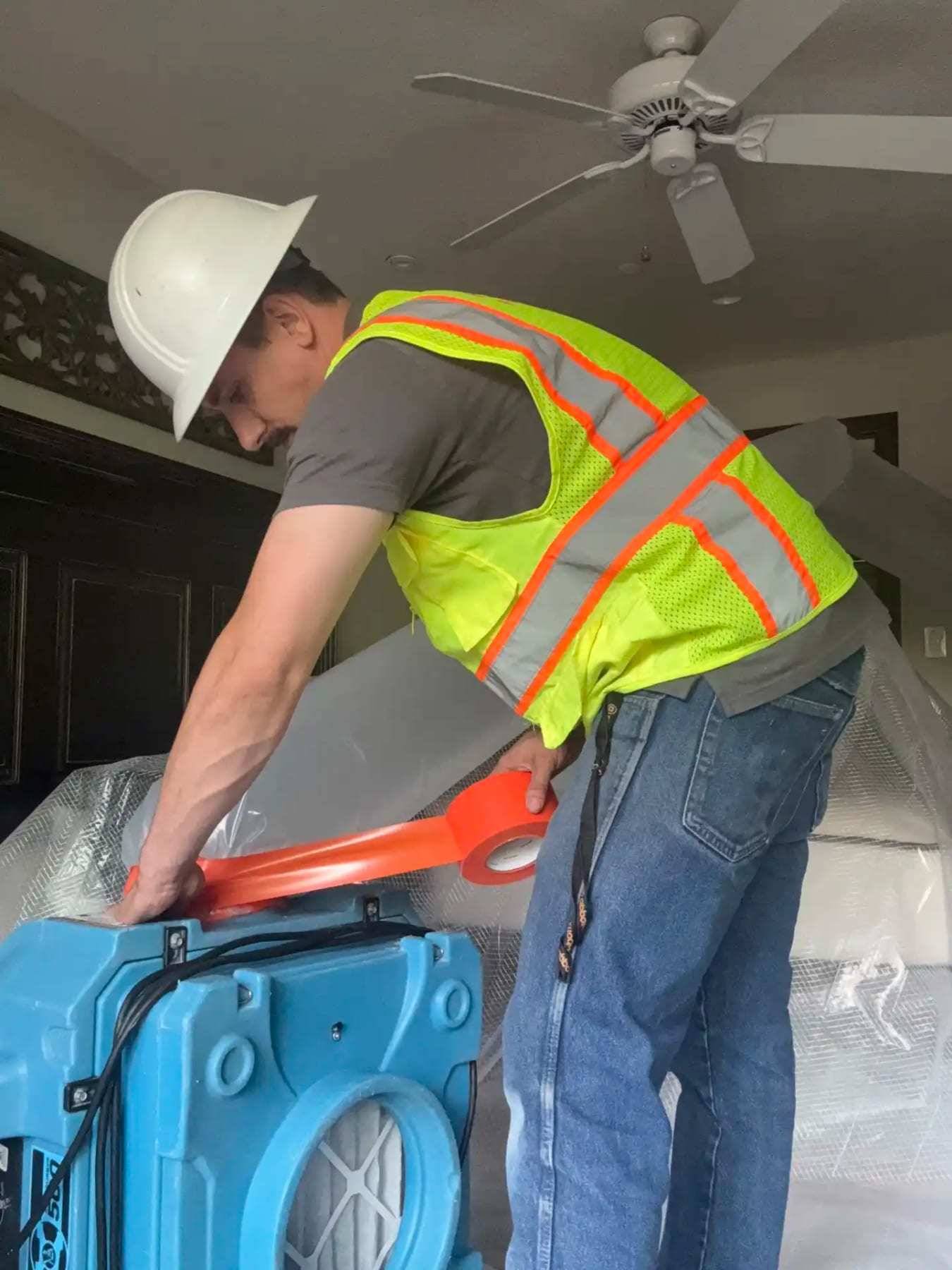 Worker in a hard hat and safety vest carrying an air mover
